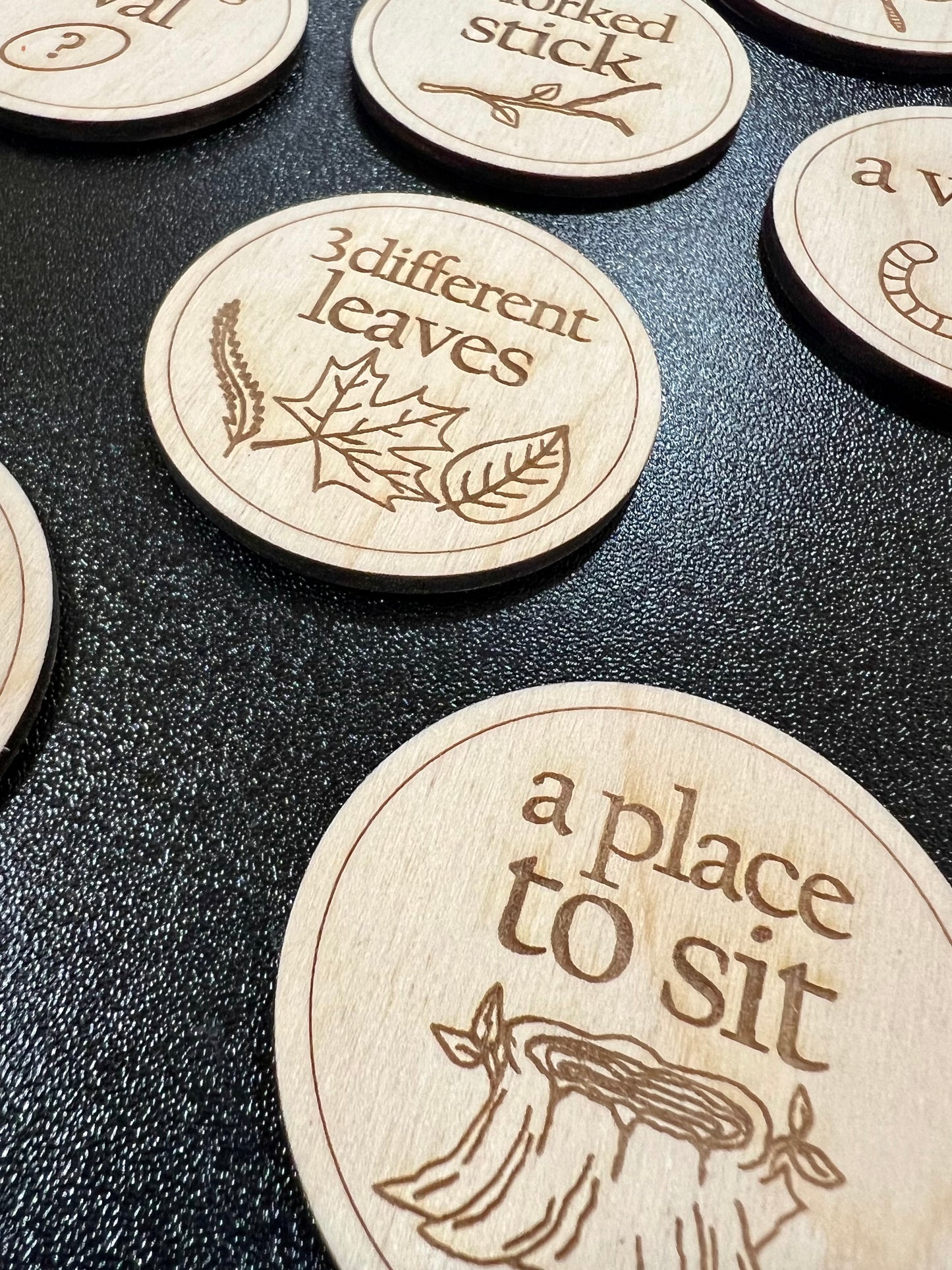 Wooden scavenger hunt coins with engraved text and illustrations are displayed on a dark surface.