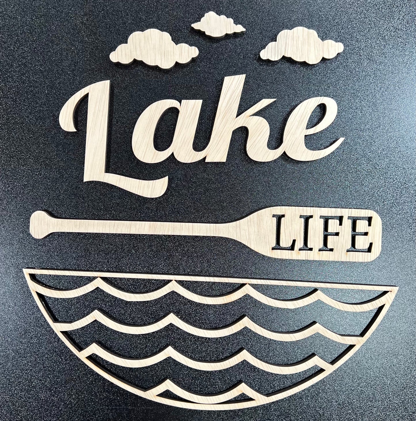 Unpainted wooden "Lake Life" sign with clouds, a paddle, and waves.