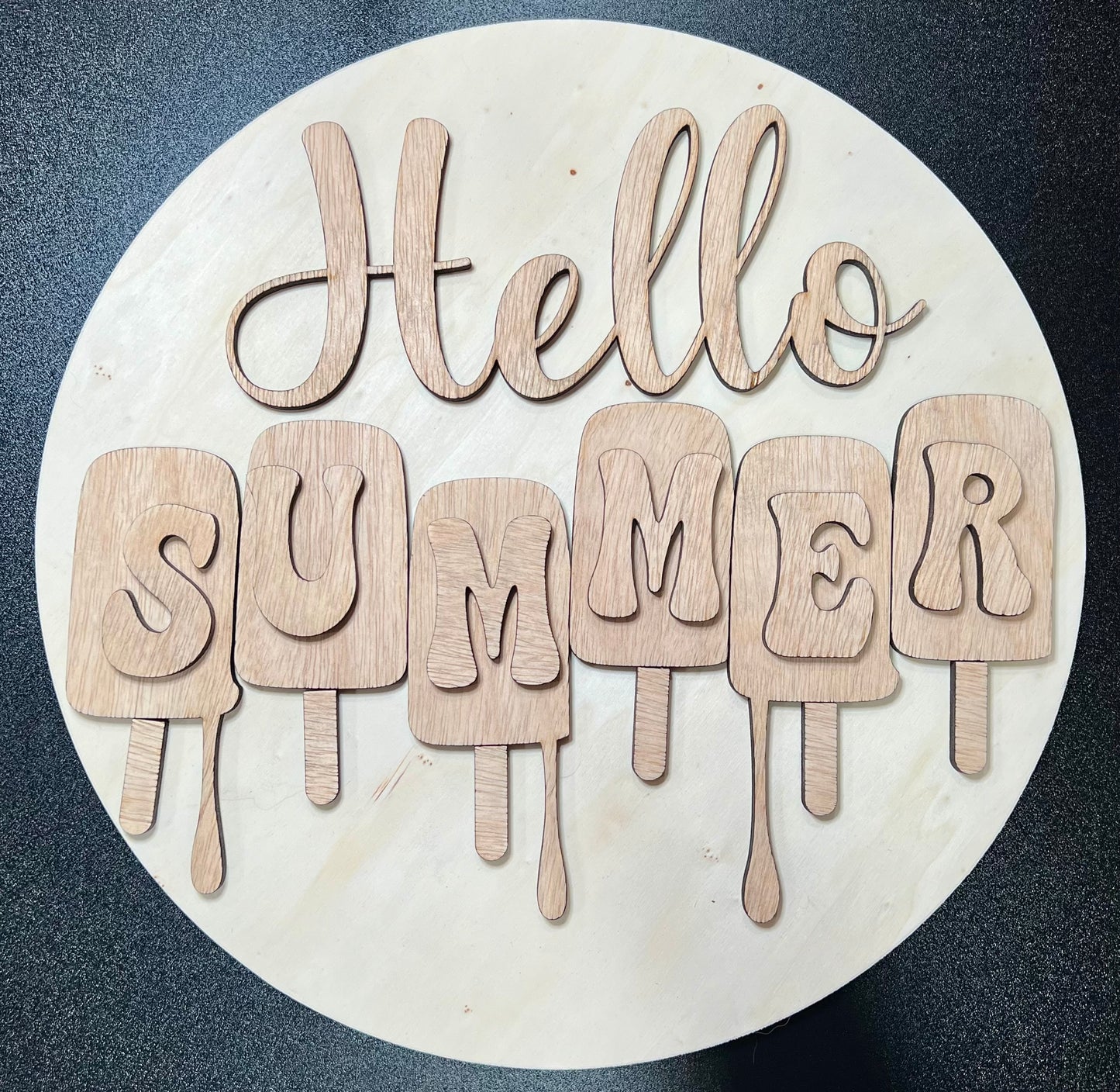 Unpainted wooden "Hello Summer" sign with popsicle-shaped letters on a round board.
