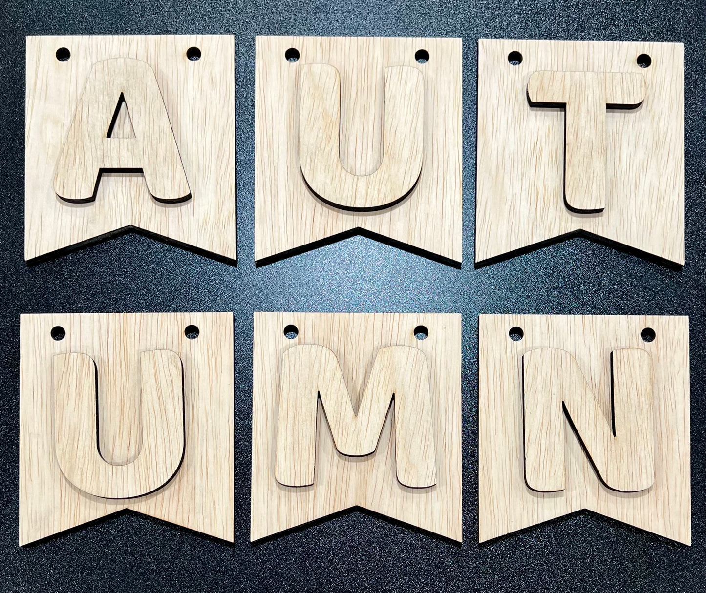 An unpainted wooden banner kit spells "AUTUMN" with raised letters on six pennants.