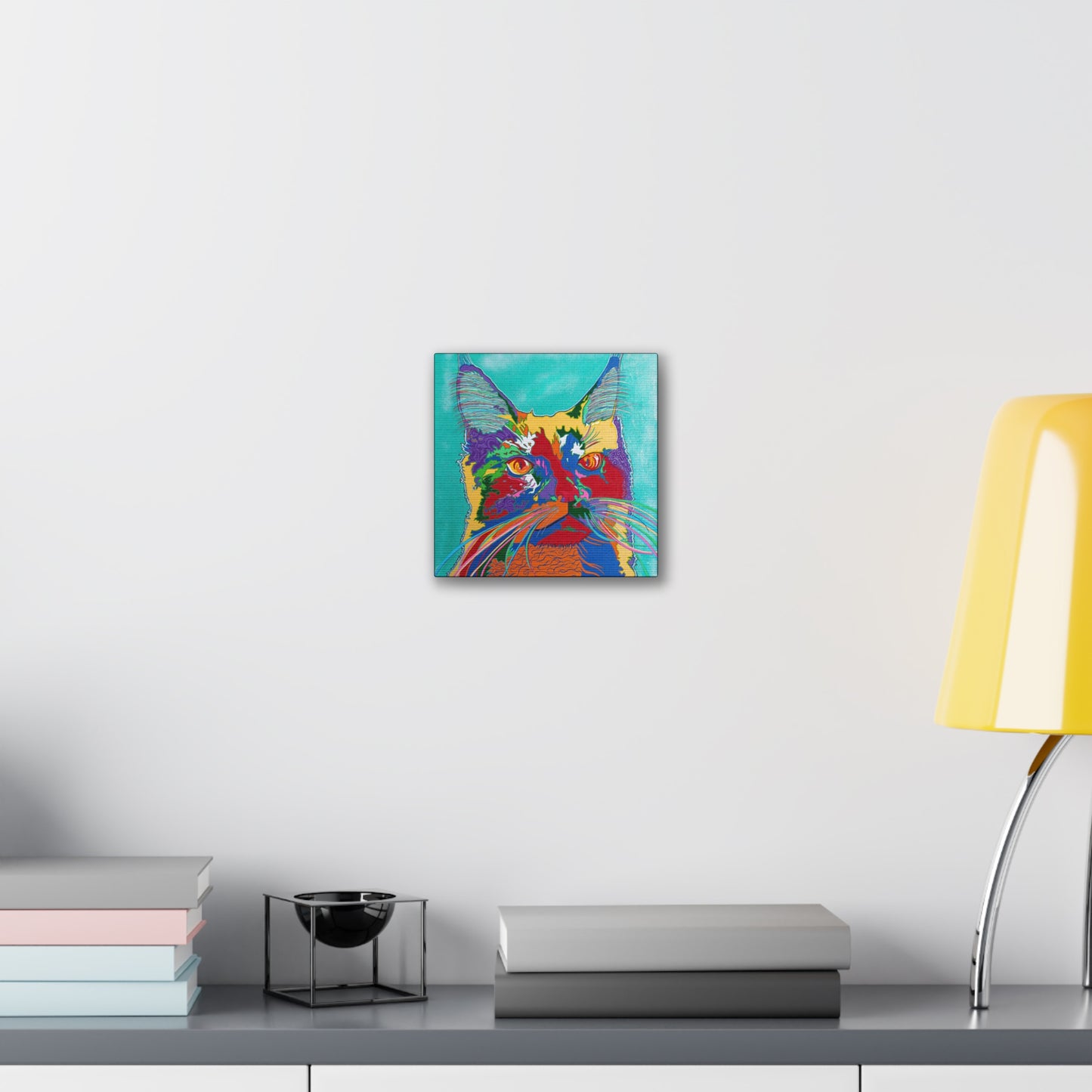 A vibrant, pop art style cat portrait hangs on a white wall above a grey shelf.