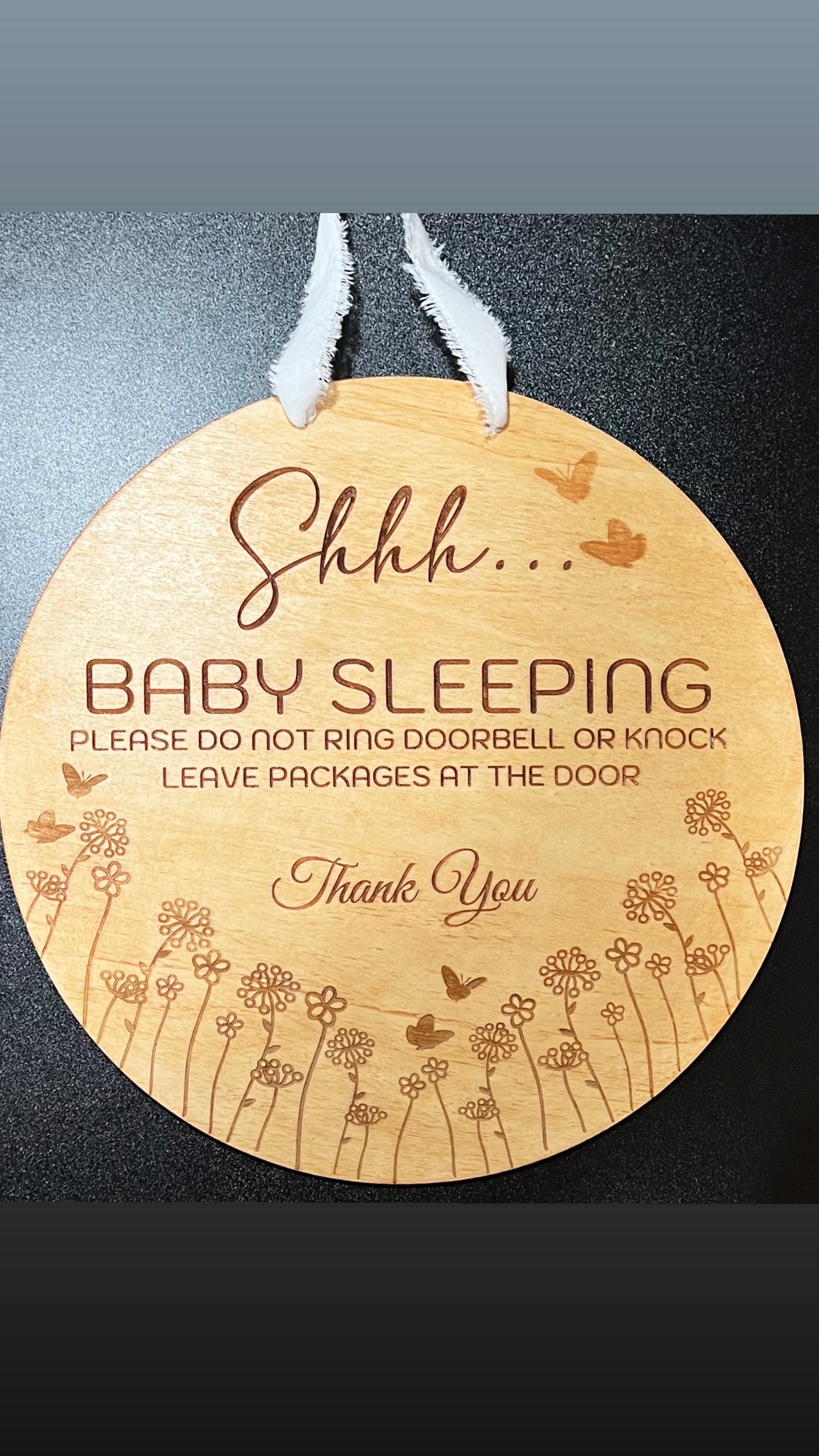 A 15-inch round wooden baby door sign with laser-engraved text and floral designs.