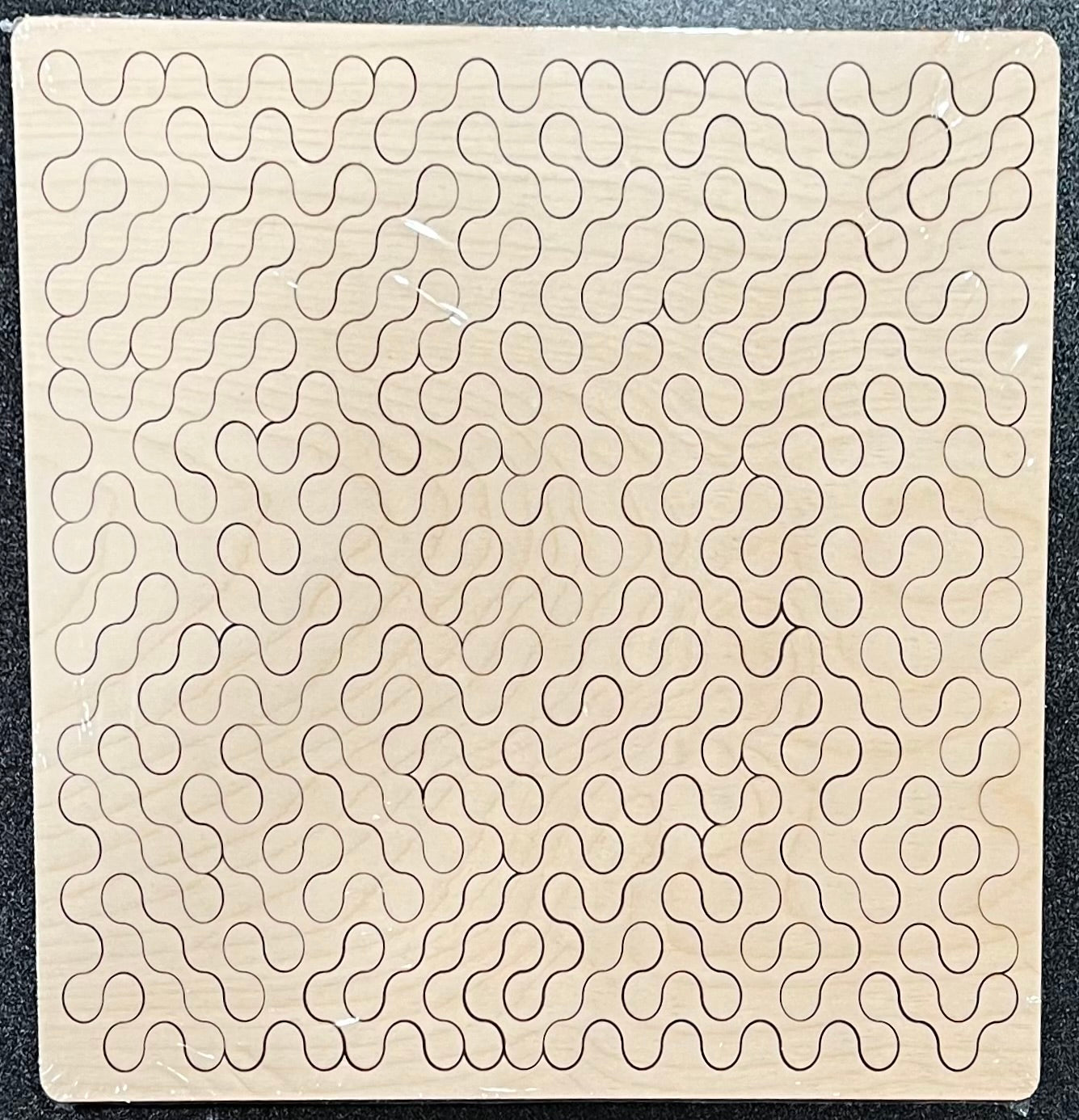 Unfinished wooden puzzle with a repeating wavy, interconnected pattern.