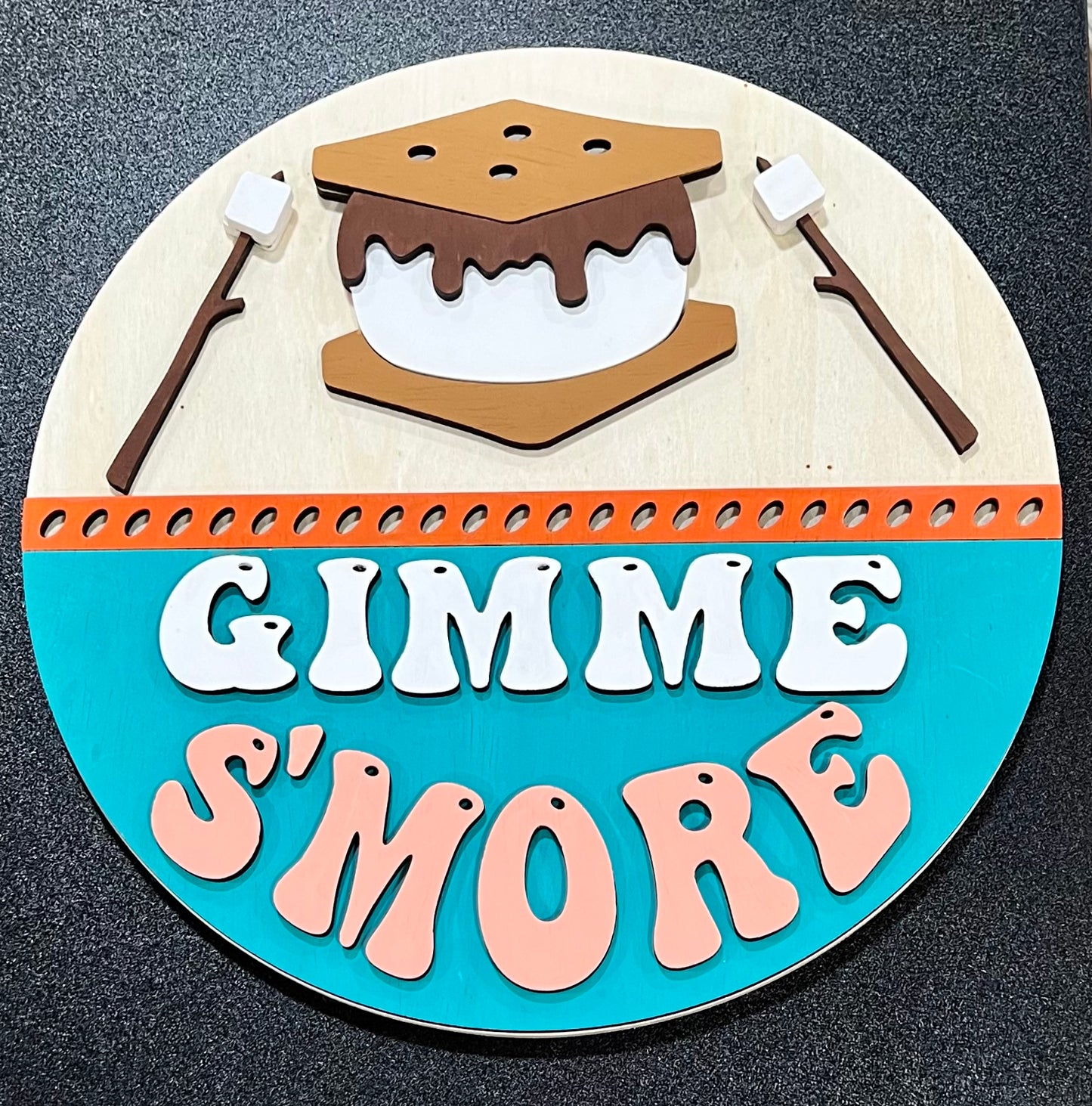 A round wooden sign features a s'more and the words "Gimme S'more".