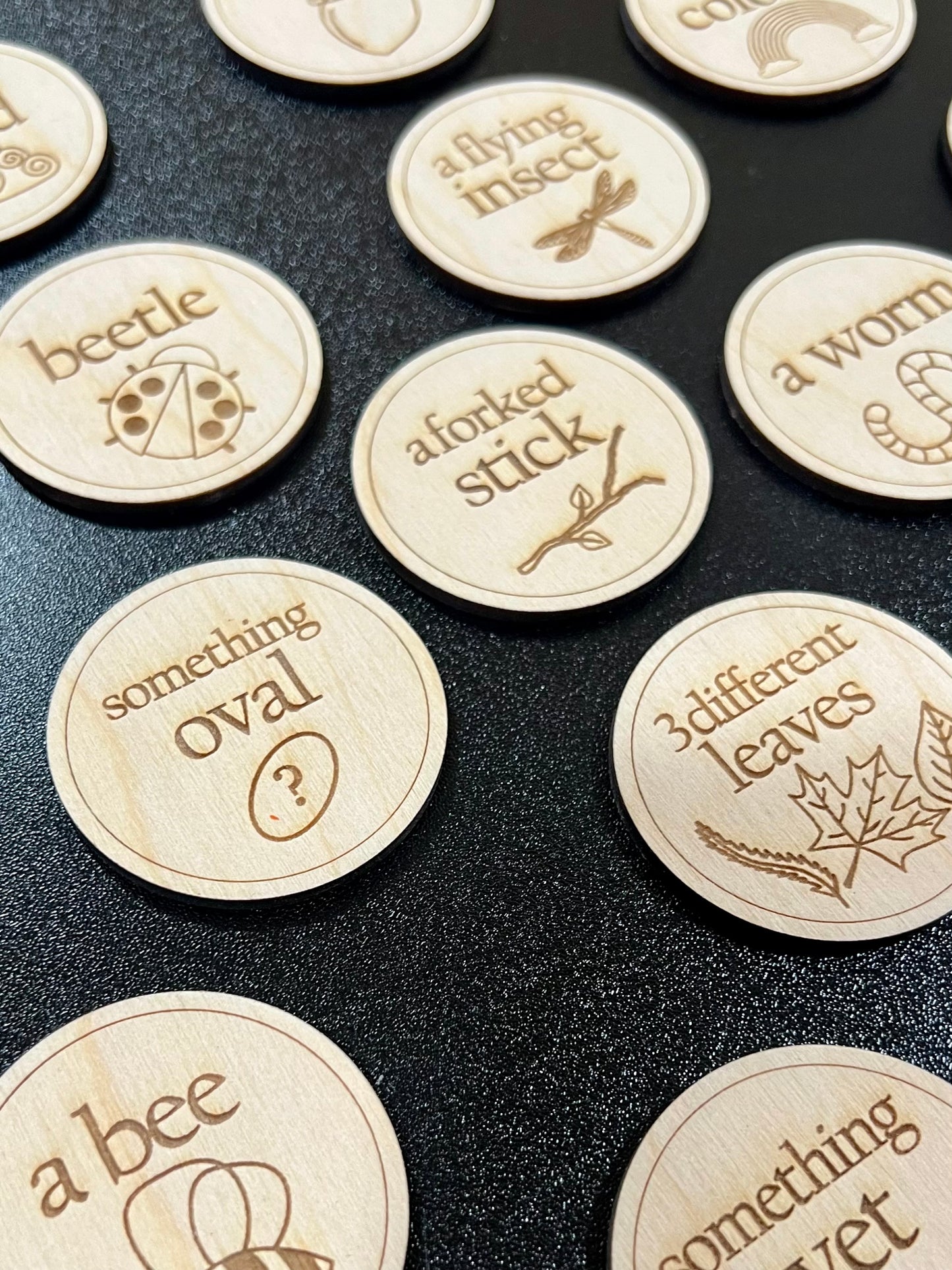 Wooden scavenger hunt coins with engraved nature-themed clues are scattered on a dark surface.