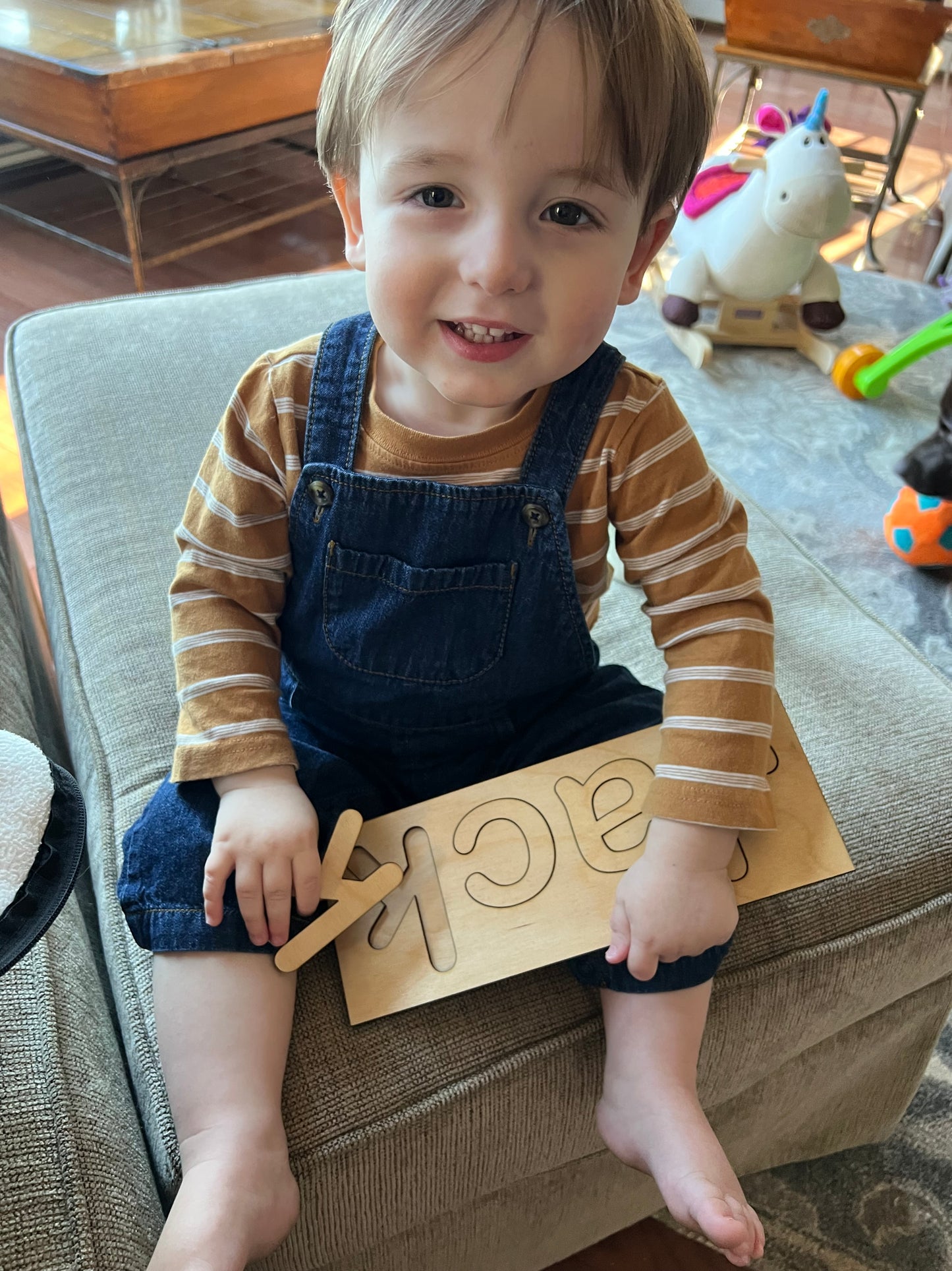 A young child sits holding a wooden name puzzle that spells "JACK".
