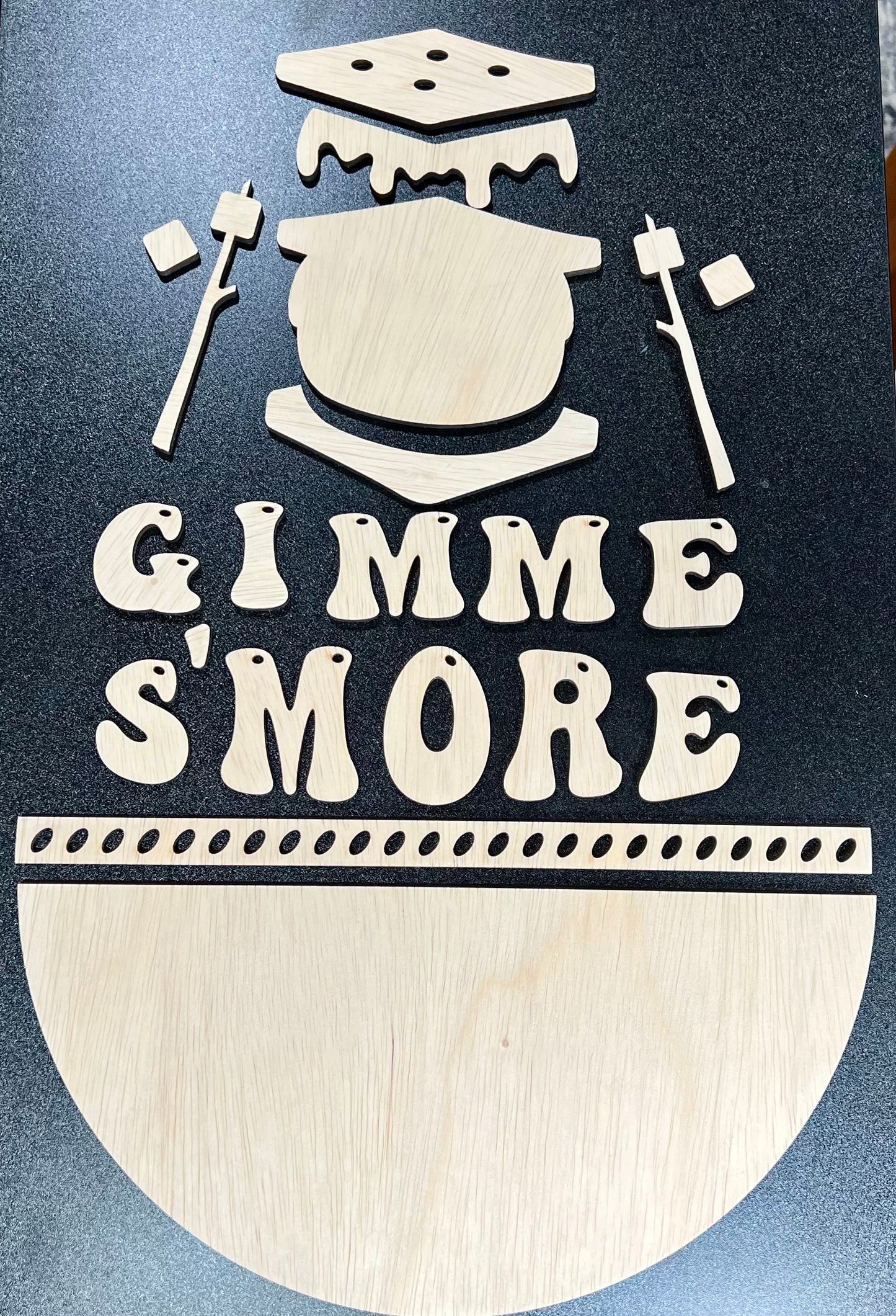 Unpainted wood sign kit spelling "Gimme S'more" with s'mores and campfire elements.