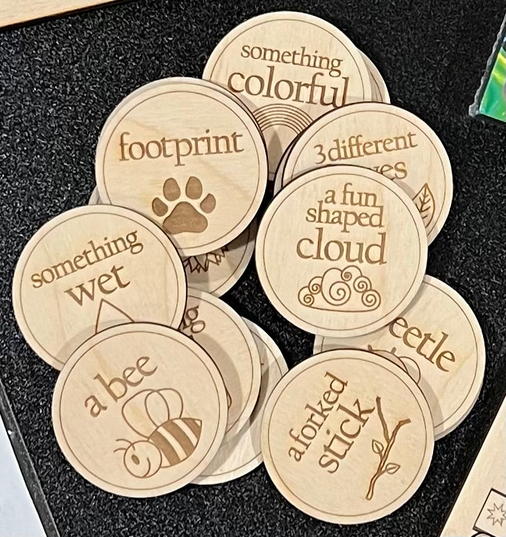 A pile of round wooden scavenger hunt coins with various engraved prompts.