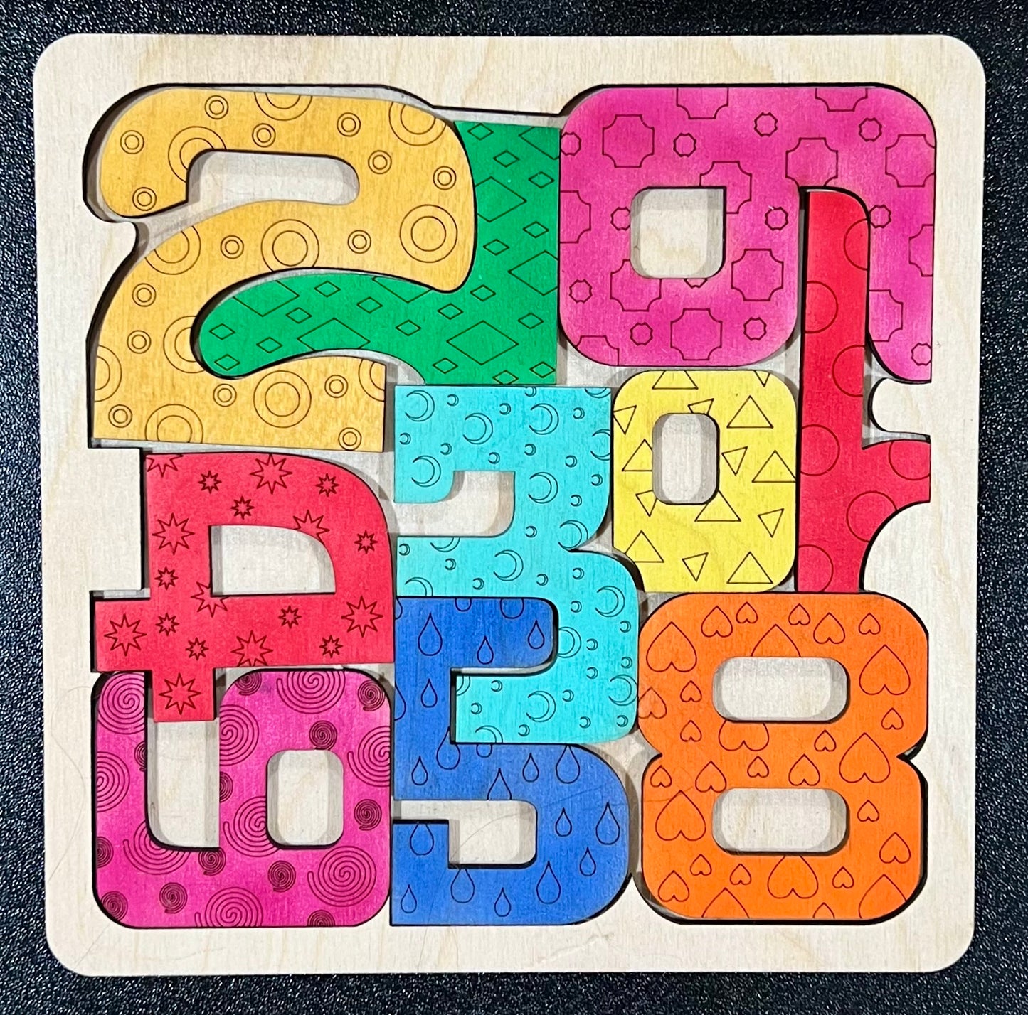 A wooden square puzzle with colorful, patterned number pieces from 0 to 9.