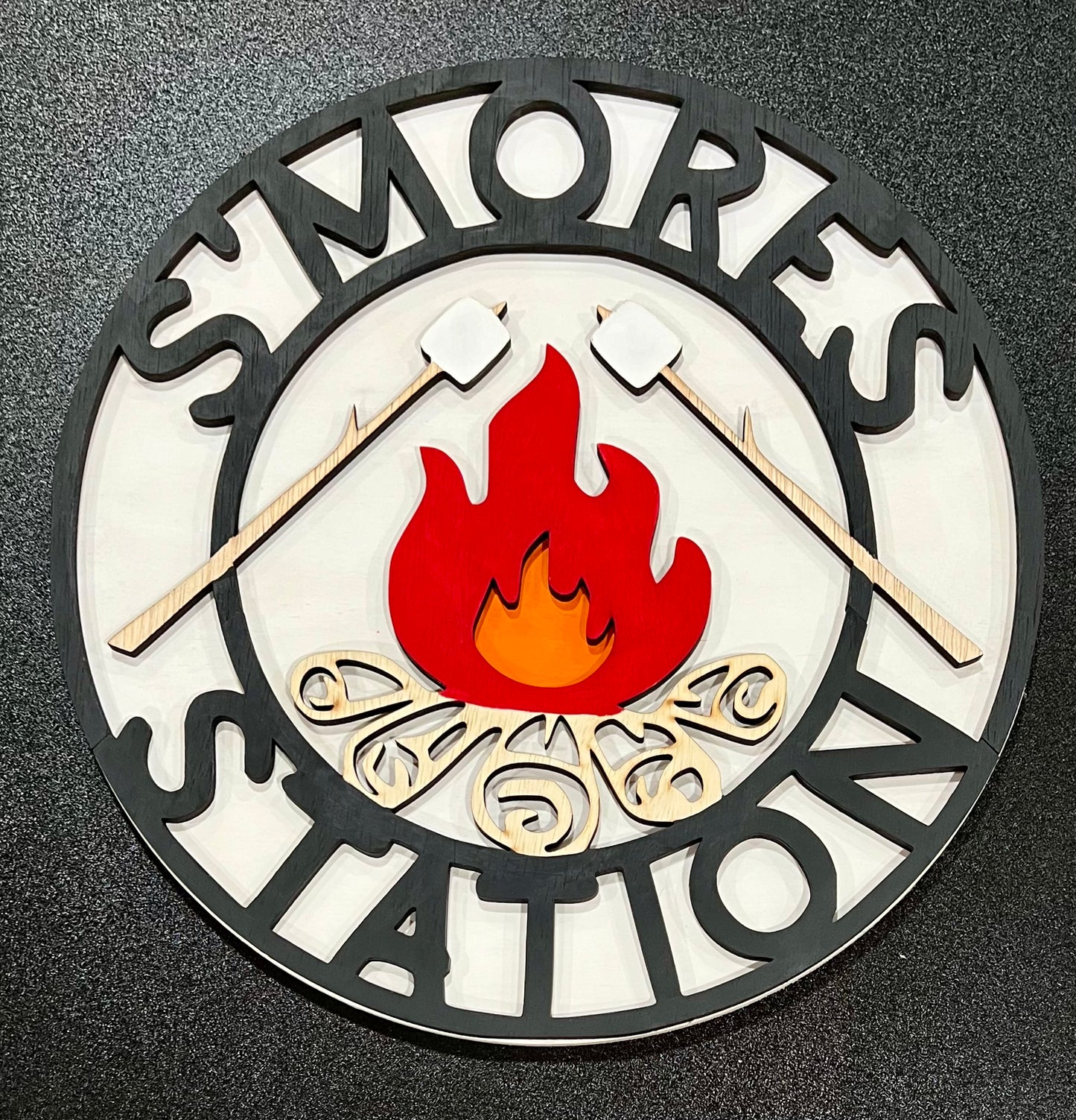 A round wooden sign reads "S'mores Station" with a campfire and marshmallows on sticks.