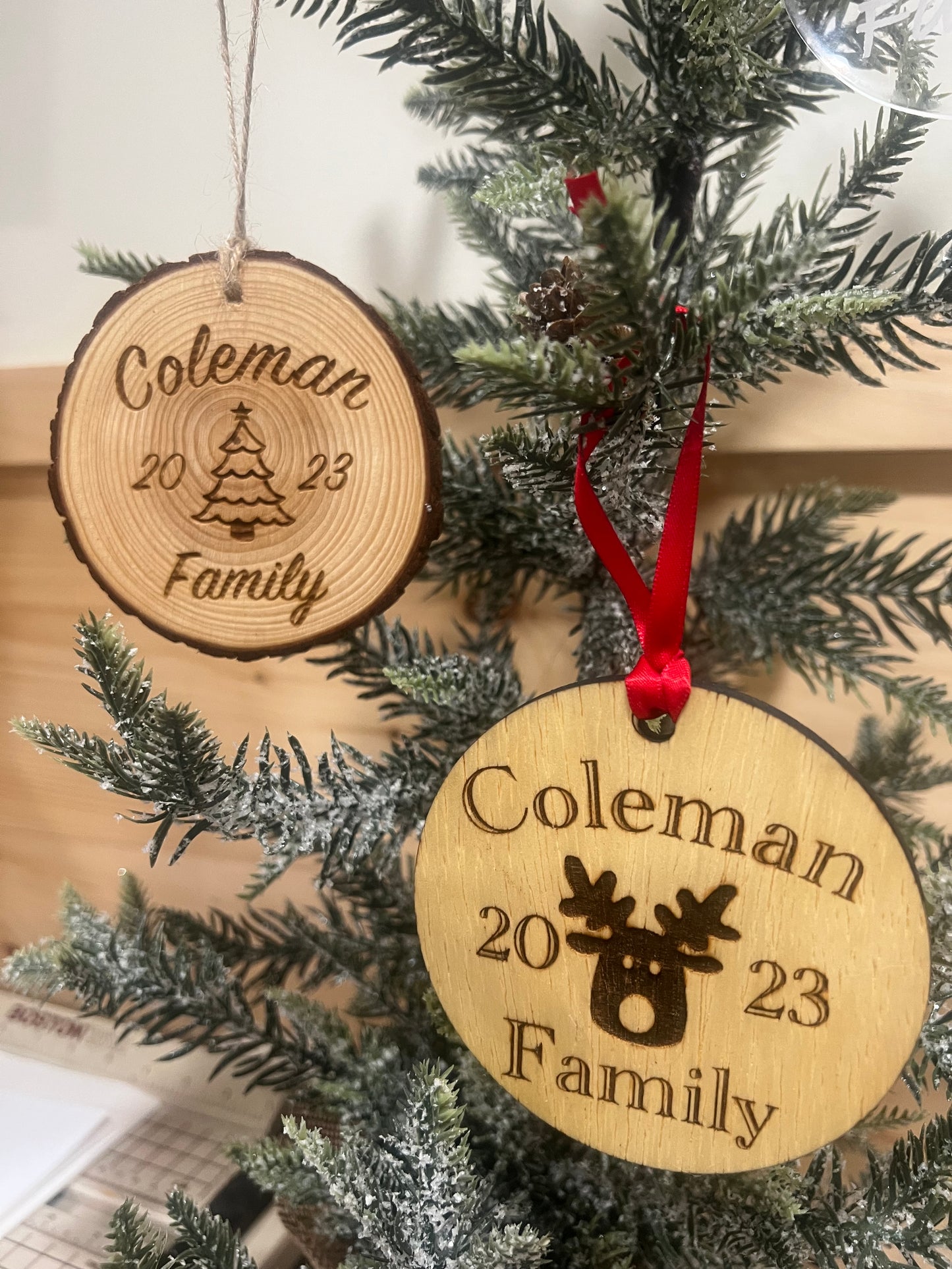 Two personalized wooden ornaments, one round and one log-cut, hang on a frosted Christmas tree.