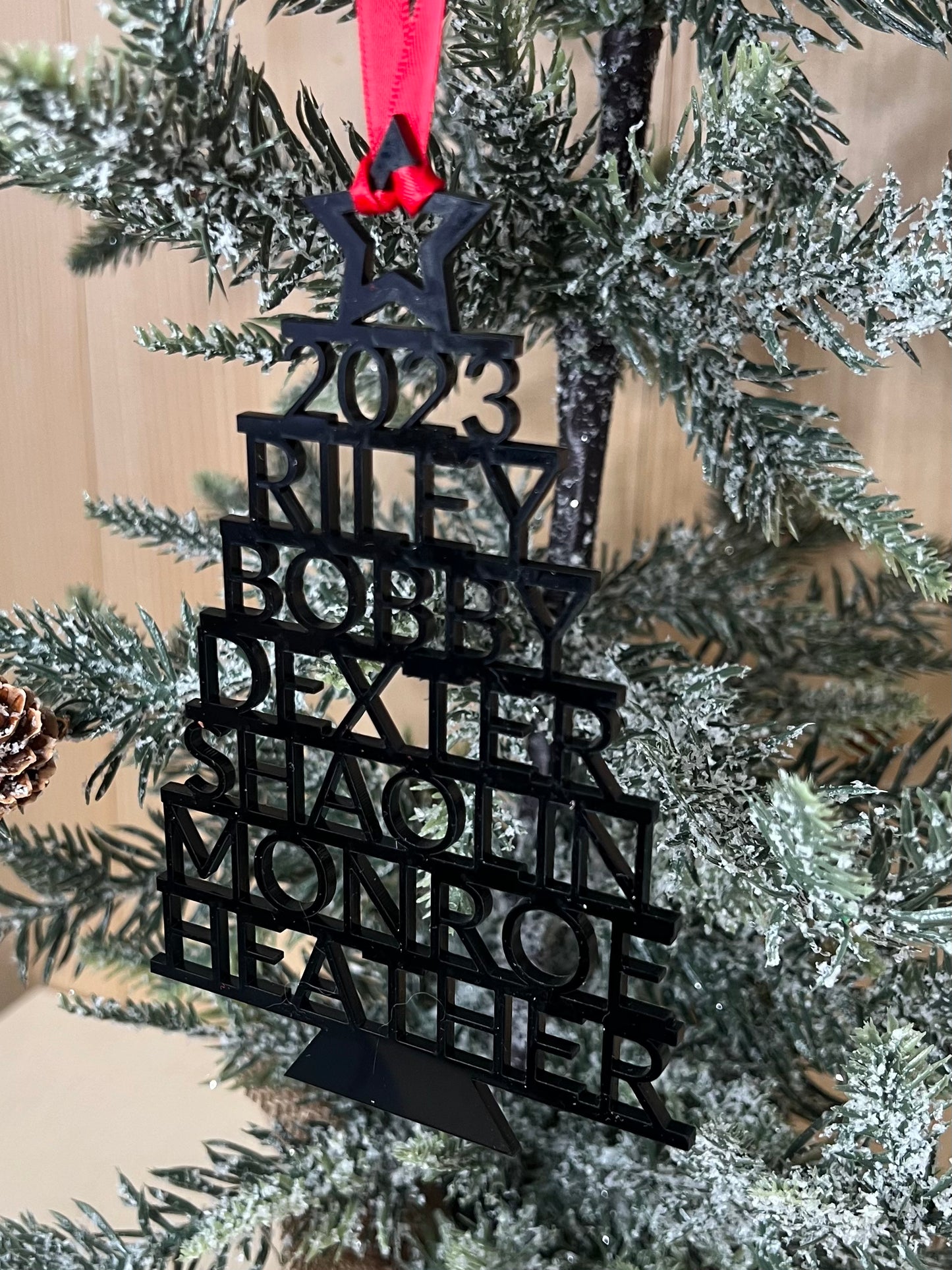 Black 2023 stacked name ornament hanging on a flocked Christmas tree.