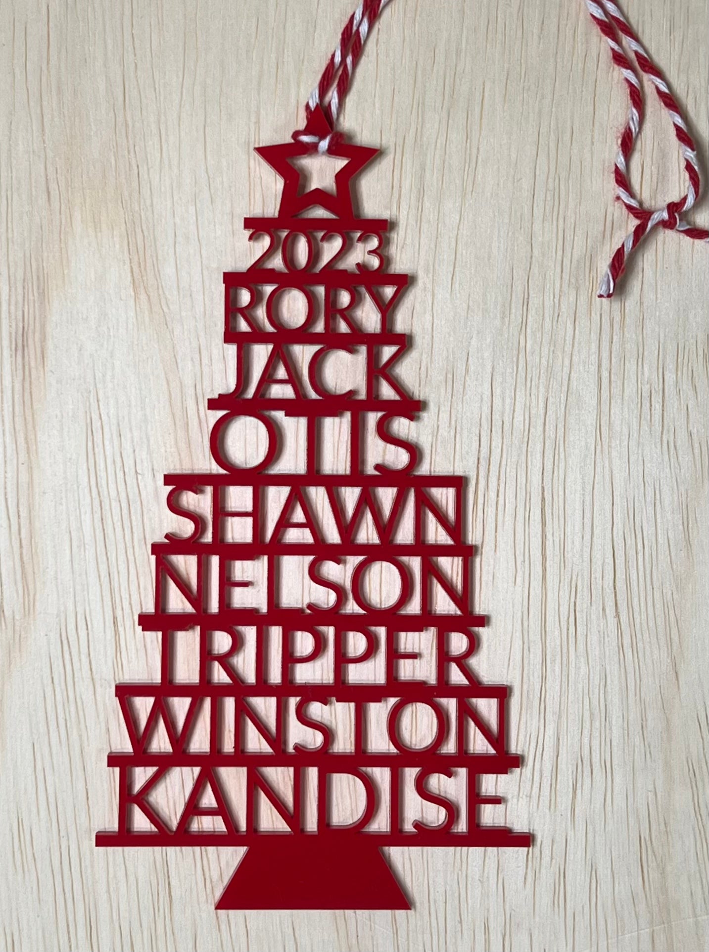 A red Christmas tree ornament with "2023" and nine names stacked vertically.