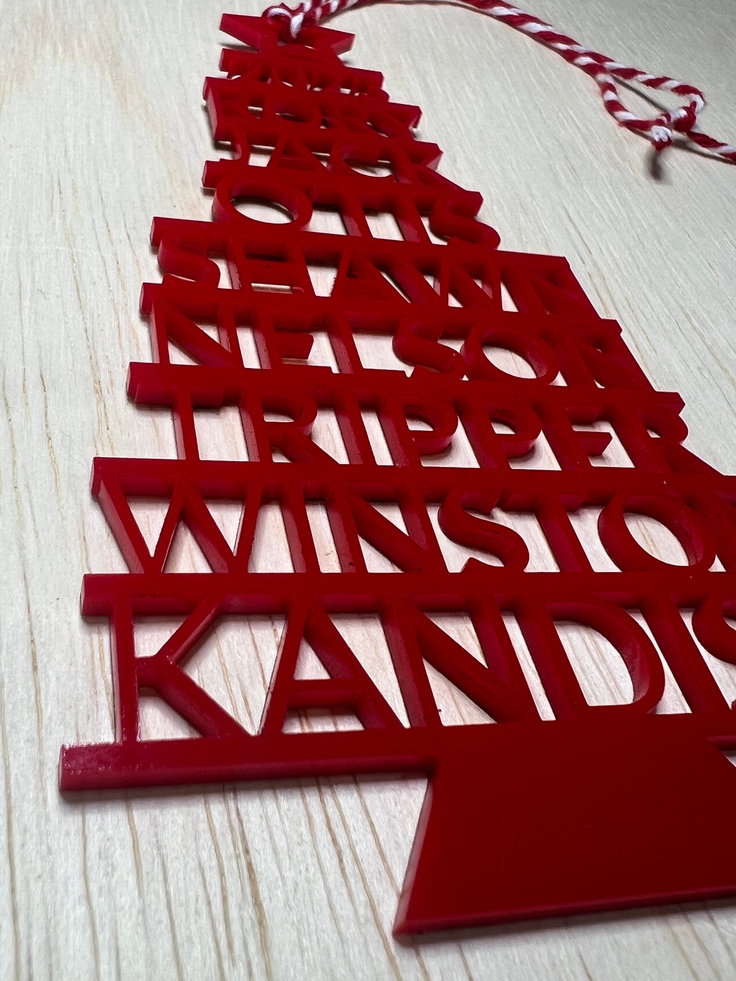 Red acrylic Christmas tree ornament with stacked family names and a red and white string.
