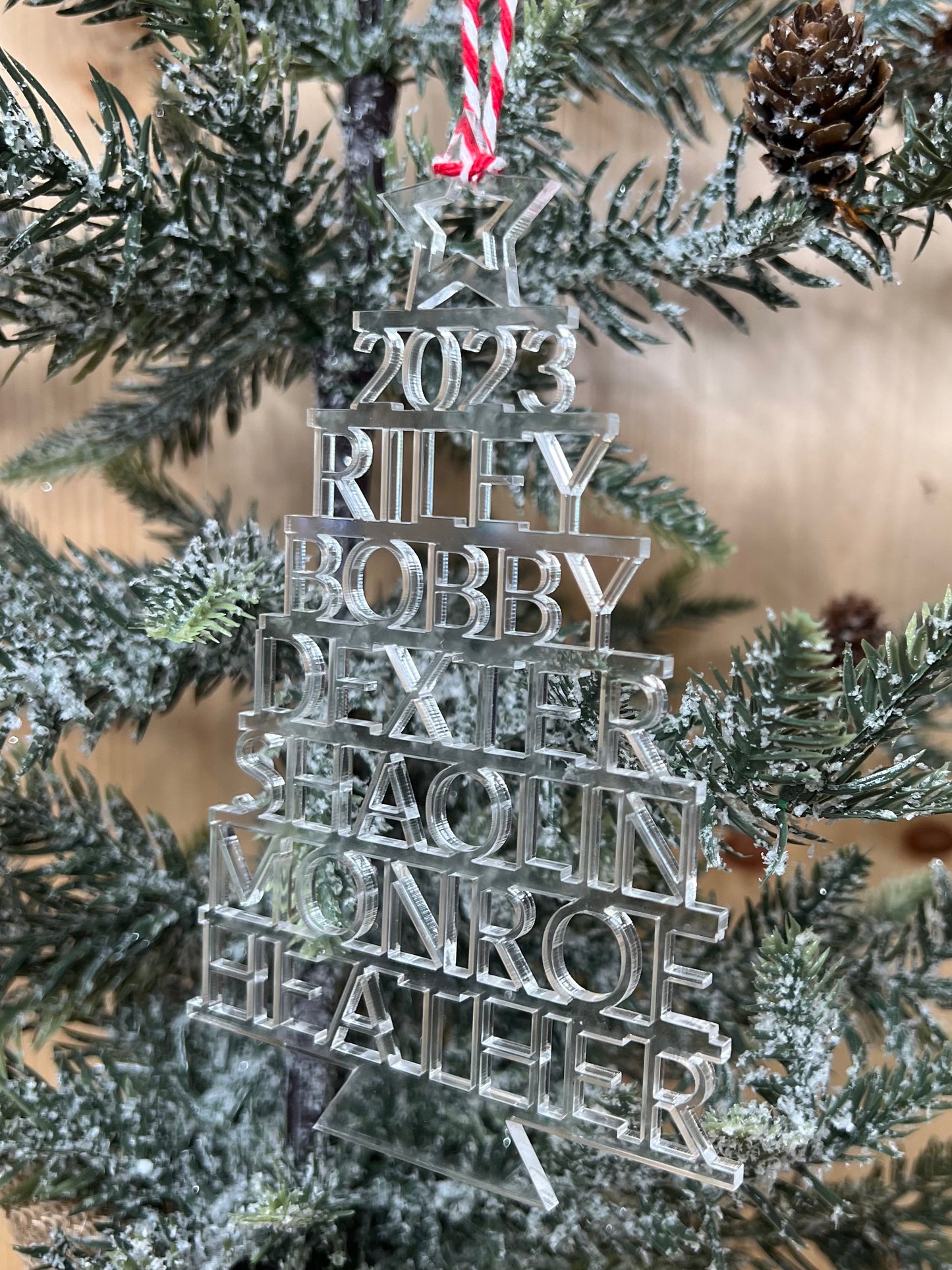 A clear acrylic Christmas ornament with stacked names and the year 2023.