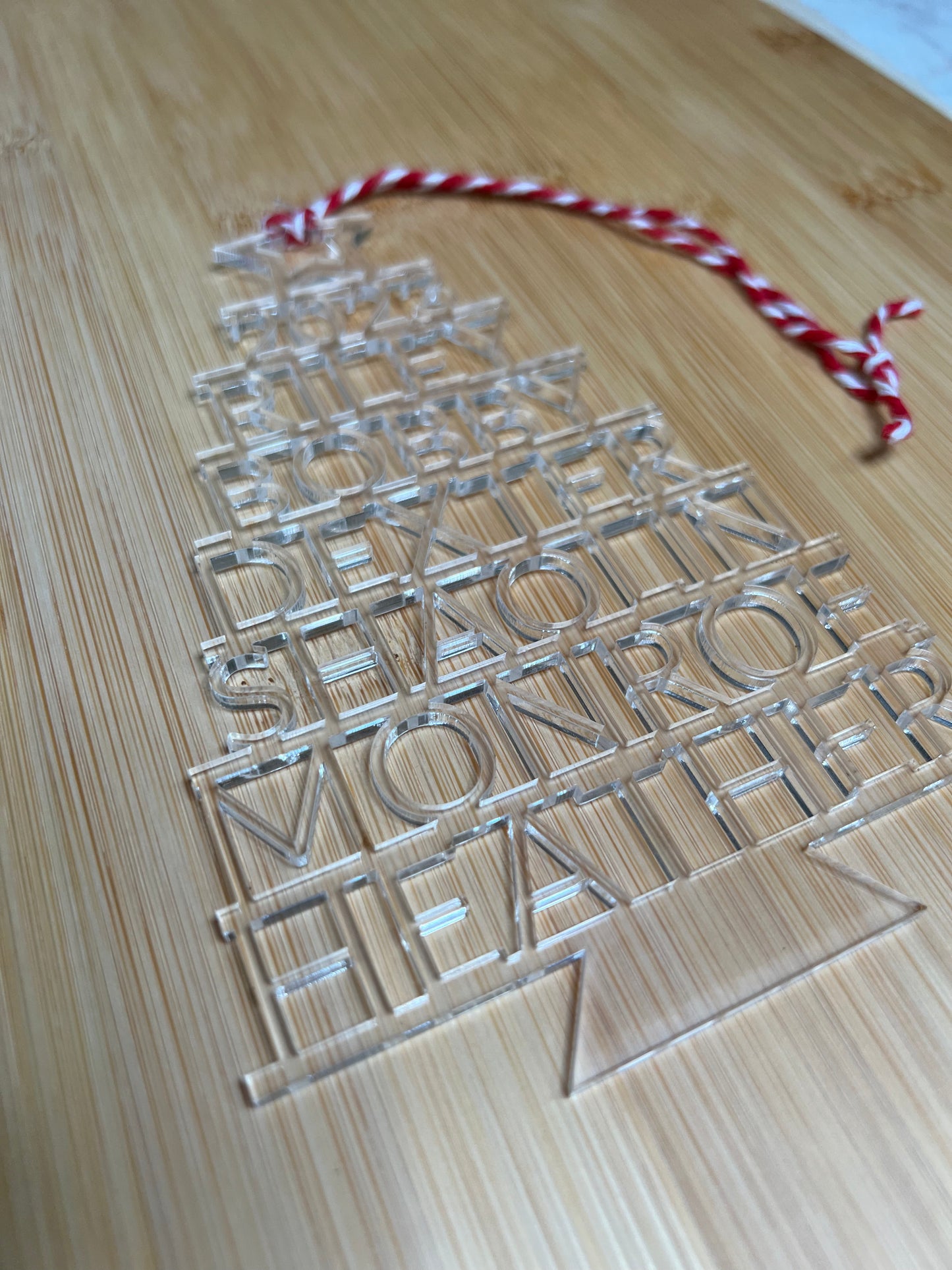 Clear acrylic Christmas tree ornament with stacked family names and a red and white string.