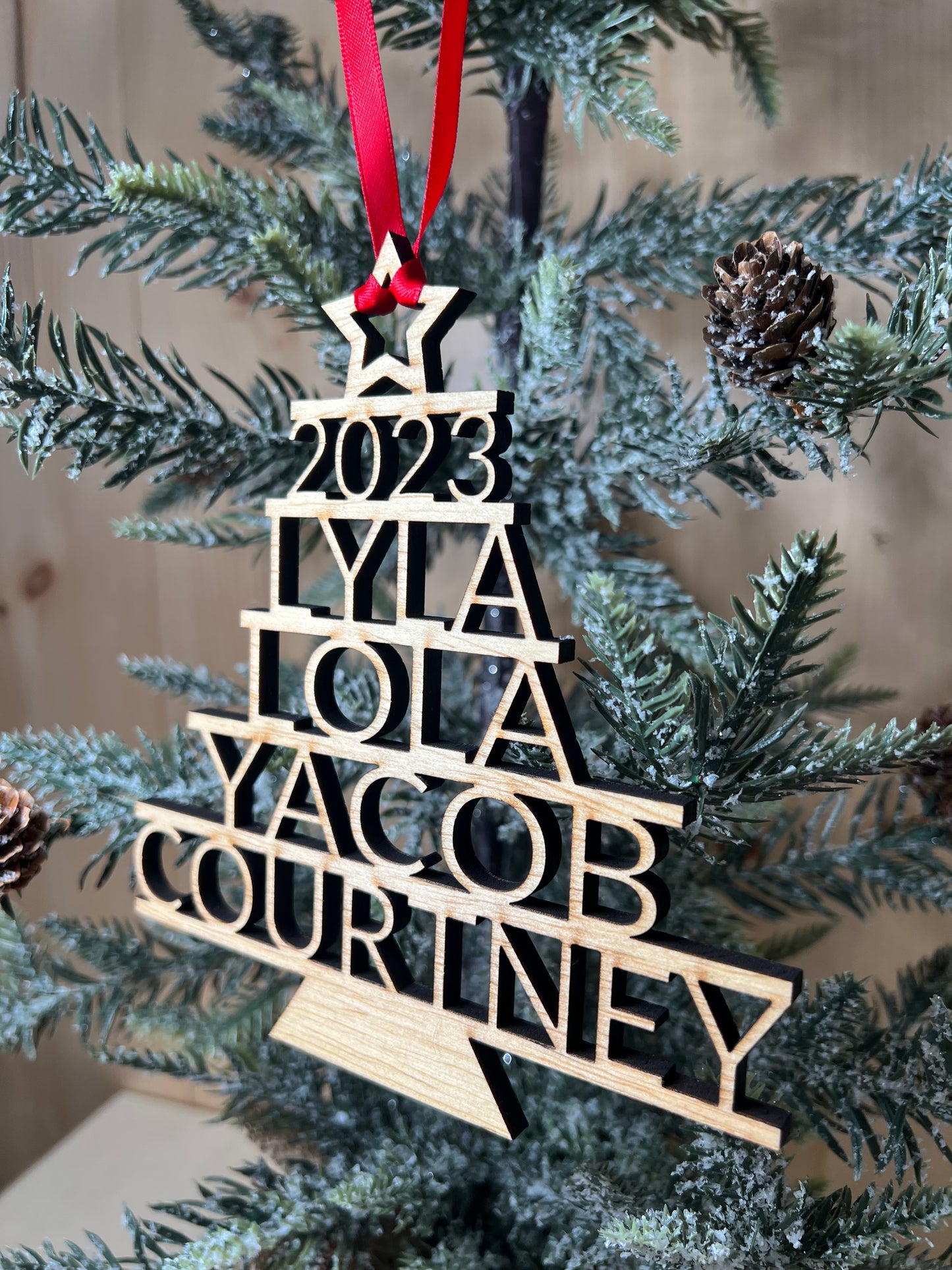 A wooden Christmas tree ornament with stacked names and the year 2023.