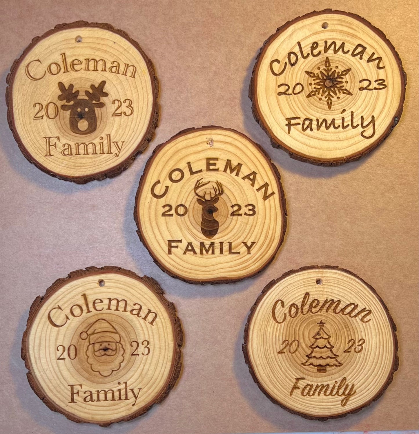 Five personalized wood slice ornaments, each engraved with "Coleman 2023 Family" and a holiday design.