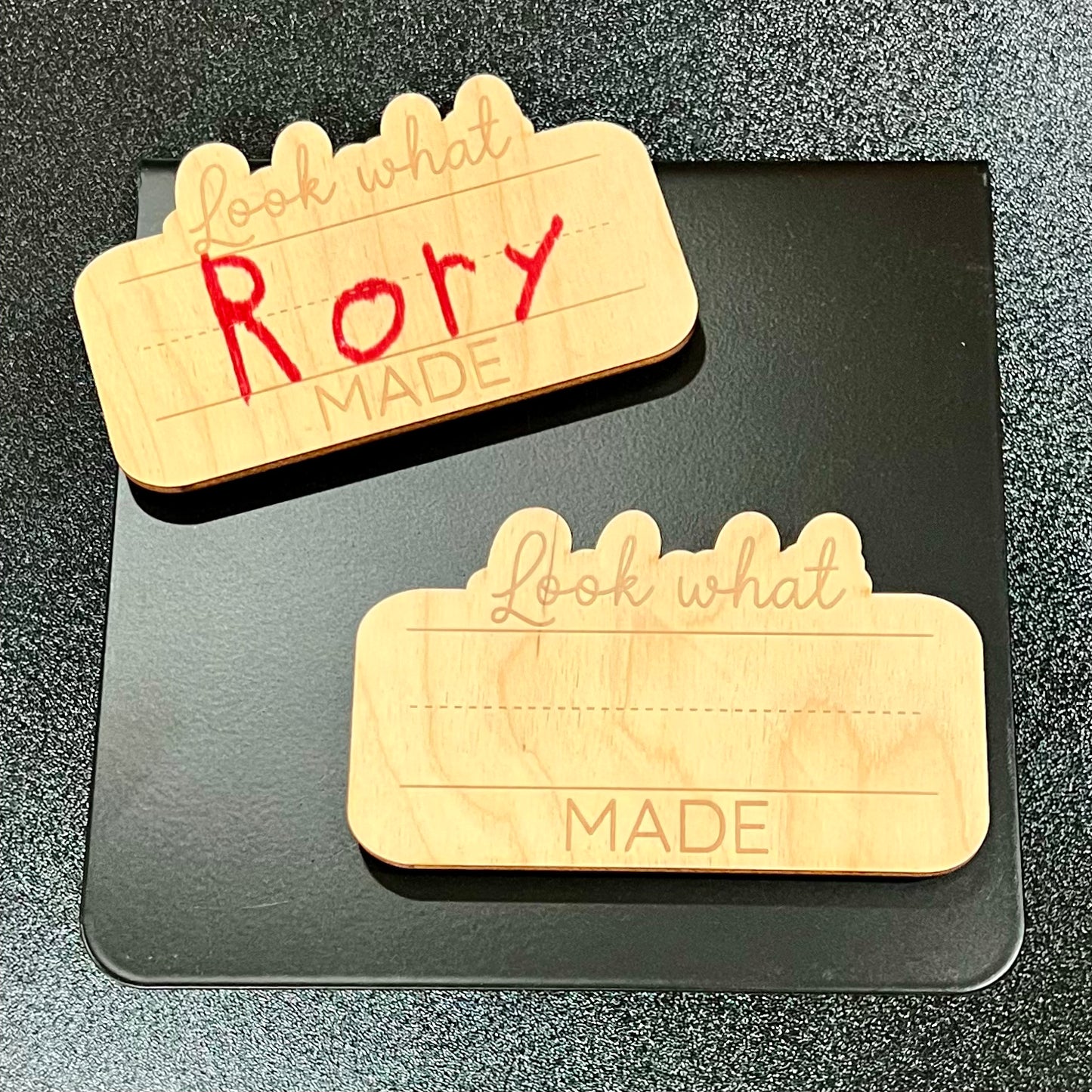 Two wooden "Look What _ Made" magnets, one with "Rory" written in red, on a black surface.