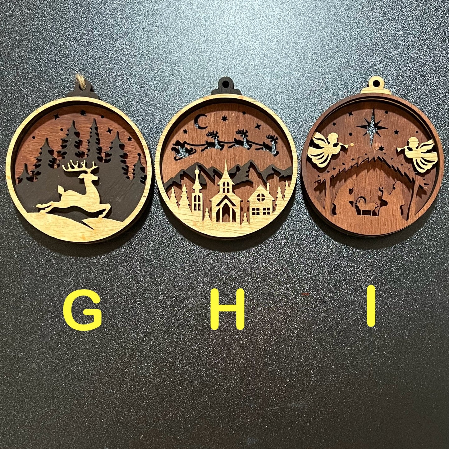Three layered wood Christmas ornaments, each with a unique holiday scene.